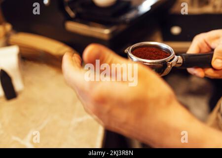 Nahaufnahme der Kaffeemühle in einem Café. Der Barista mahlt frisch geröstete Kaffeebohnen mit einem professionellen, modernen elektrischen Grinsen Stockfoto