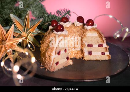 Deutsche Kuchen Frankfurter Kranz oder Frankfurter Crown Cake. Bisquit mit Buttercreme, Kirsche. Die Hälfte des Kuchens auf schwarzem Teller. Schwarzer und rosafarbener Hintergrund Stockfoto