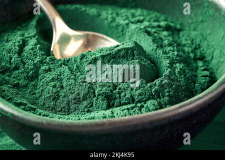 Grünes Spirulinapulver in einer schwarzen Schüssel mit einem Löffel Stockfoto