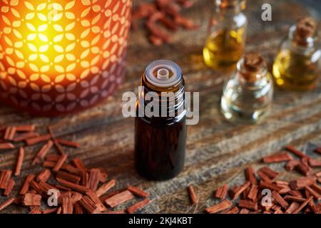 Eine dunkle Flasche ätherisches Aromatherapieöl mit roten Sanalholzchips, mit Kerzenlicht im Hintergrund Stockfoto