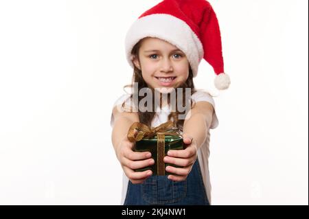 Konzentrieren Sie sich auf die Hände eines verschwommenen, reizenden kleinen Mädchens mit Weihnachtsmannmütze, überreichen Sie ein niedliches Weihnachtsgeschenk, isolierter weißer Hintergrund Stockfoto