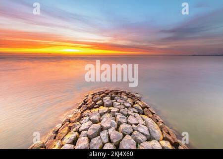 Typischer Bau von Basalt-Wellenbrechern am IJsselmeer in der Nähe der Stadt Hindeloopen in der Provinz Friesland bei Sonnenuntergang, Niederlande. Stockfoto