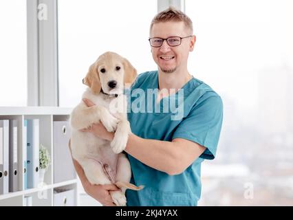 Gutaussehender Tierarzt hält gesunden jungen Hund in der Klinik Stockfoto