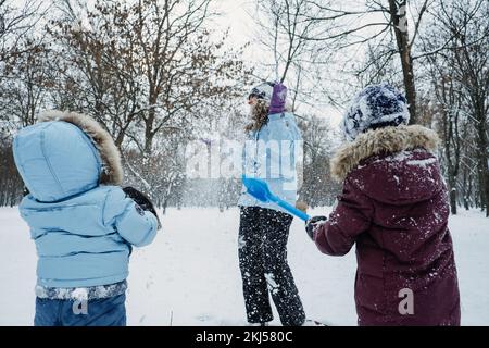Fröhliche Familie, Freunde, Mutter und Kinder, die im Winter im verschneiten Naturklang Spaß im Freien haben. Mom und zwei Jungs spielen Schneeball im Winter Park draußen Stockfoto