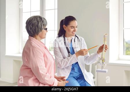 Der Arzt während der Sprechstunde für ältere Frauen zeigt Modelle der Wirbelsäule, während er über die Behandlung spricht. Stockfoto