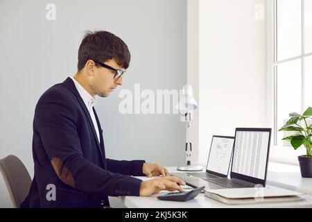 Buchhalter verwendet Taschenrechner und arbeitet mit digitalen Geschäftsdokumenten auf Laptops Stockfoto