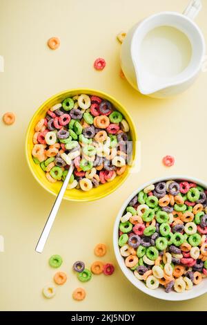 Bunte Maisringe in Schale auf gelbem Hintergrund. Ringförmige süße Frühstücksflocken mit Milch. Stockfoto