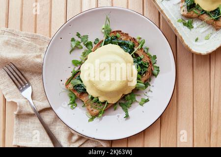 Vegane Eier benedict-Gericht mit Sauerteigbrot, cremiger Sauce auf Pflanzenbasis Hollandaise, geräuchertem Tofu, jungen Zwiebeln, Petersilie, Gemüse, erbsensprossen Stockfoto