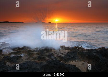 Bild des Sonnenaufgangs mit Wellen auf den Felsen am Strand von Bombay, Santa Eulalia, Ibiza, Spanien. Stockfoto