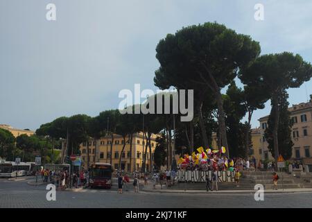 Eine Gruppe von Demonstranten auf einem stadtplatz in der Nähe eines Busbahnhofs mit italienischen Steinkiefern in Rom, Italien. Kleiner Protest tagsüber. Stockfoto