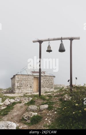 Alte orthodoxe Kirche St. Giorgi in der Khvamli Gebirgskette in Georgien mit einfachem Holzglockenturm mit zwei Glocken, nebiges Wetter. Stockfoto