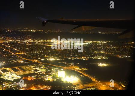 Nachtstadt aus dem Fenster des Flugzeugs. Große Metropole in goldenen Lichtern. Der Schwanz eines Flugzeugs ist am Nachthimmel zu sehen. Wunderschöne Landschaft. Stockfoto