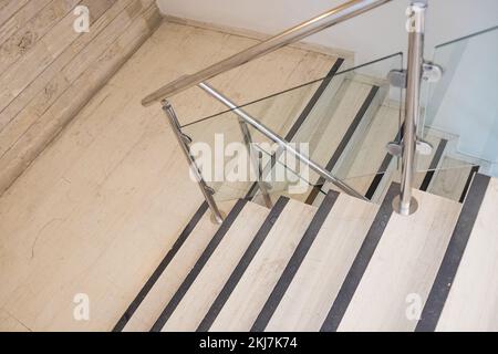 Moderne Architektur mit Marmortreppen. Marmortreppe mit gläsernen Handläufen. Weiße Treppe führt nach unten. Moderne Innentreppe mit Glas Stockfoto