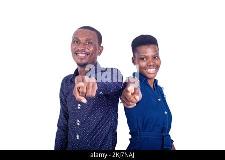 Ein junges Paar, das auf weißem Hintergrund steht und eine Richtung zeigt, die mit dem lachenden Finger zeigt. Stockfoto