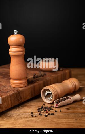 Pfeffermühle und ganzer Pfeffer in einer Holzschaufel auf einem Holztisch. Stockfoto