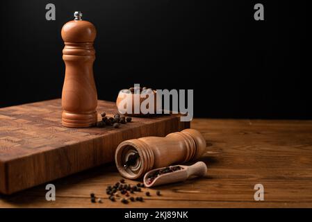 Pfeffermühle und ganzer Pfeffer in einer Holzschaufel auf einem Holztisch. Stockfoto