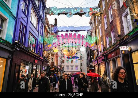 London, Großbritannien. 24.. November 2022. Einkaufslustige können bei nassem Wetter durch die Weihnachtslichter in der berühmten Carnaby Street von Soho schlendern und sie genießen. Die diesjährige Installation heißt „Carnaby Celebrations“ und feiert 25 Jahre der Weihnachtslichter der Carnaby Street. Kredit: Imageplotter/Alamy Live News Stockfoto