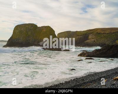 Große, grüne moosbedeckte Felsbrocken im Ozean. Gewitterwolken am Himmel. Düstere Meereslandschaft. Natur, Geologie, Wetter, Klima, Umweltschutz Stockfoto