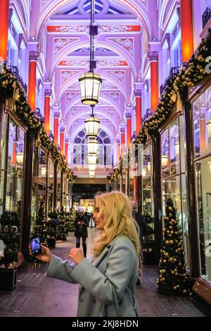 London, Großbritannien. 24.. November 2022. Shopper machen Fotos mit den hübschen Lichtern in der Royal Arcade. Menschen in der Bond Street, Mayfair's berühmter Einkaufsstraße, und entlang Piccadilly stöbern durch die Schaufenster und bewundern die vielen bunten Ausstellungen und aufwändigen Weihnachtsdekorationen in den Luxusgeschäften von Mayfair. Kredit: Imageplotter/Alamy Live News Stockfoto