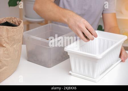 Ein Mann schläft in einer Blumenkäste aus geschäumtem Ton ein. Bodenvorbereitung, die erste Schicht Blähton. Vorbereitung für die Pflanzung von Pflanzen. Gartenarbeit zu Hause. Stockfoto