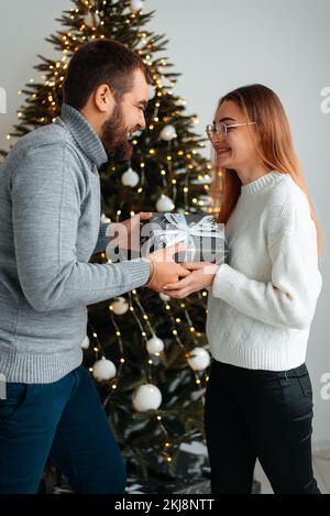 Süßes, junges Paar, das Weihnachtsgeschenke gegen Weihnachtsmorgen tauscht Stockfoto