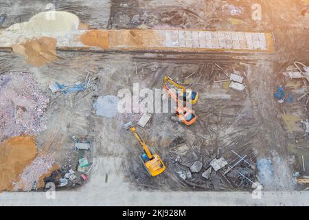 Drei Baggertraktoren auf Raupen in der Fundamentgrube während des Baus des Fundaments. Draufsicht Stockfoto