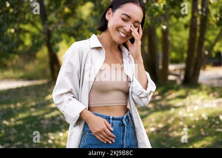 Das stilvolle asiatische Mädchen geht im Park spazieren, lacht und genießt das Sommerwetter. Menschen- und Lifestyle-Konzept Stockfoto