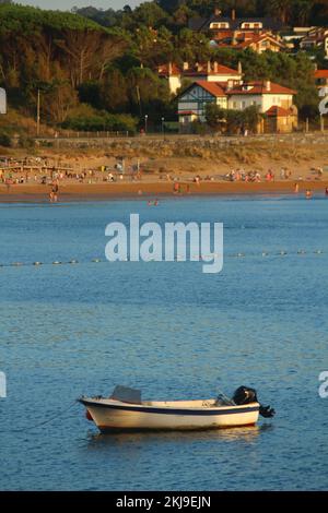 Bootstour in der Bucht von Gorliz (Baskenland) im Sommer bei Sonnenuntergang. Leute, die am Strand Spaß haben, sind im Hintergrund zu sehen, ebenso wie einige Stockfoto