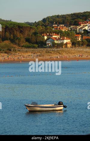 Bootstour in der Bucht von Gorliz (Baskenland) im Sommer bei Sonnenuntergang. Leute, die am Strand Spaß haben, sind im Hintergrund zu sehen, ebenso wie einige Stockfoto