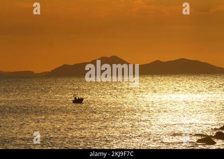 Sonnenuntergang auf dem Meer, mit der Silhouette eines kleinen Bootes, das in Sonnenspiegeln schwimmt, mit kantabrischen Bergen im Hintergrund, von Gorliz aus gesehen Stockfoto