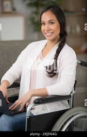 Frau im Rollstuhl zu Hause mit Laptop Stockfoto