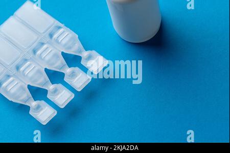 Zusammensetzung von Kochsalzlösung-Kapseln und Tropfflasche auf blauem Hintergrund mit Kopierraum Stockfoto