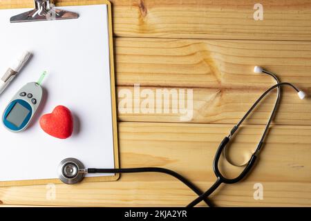 Stethoskop und Klemmbrett mit Glukometer und rotem Herzen auf Holzhintergrund mit Kopierbereich Stockfoto