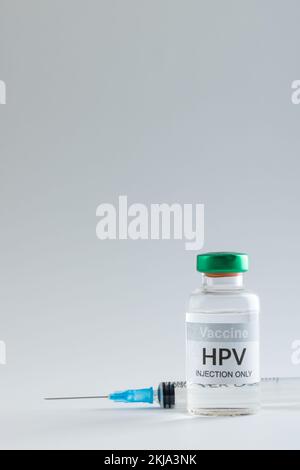 Vertikale Zusammensetzung von hpv-Impfstoff-Fläschchen und Spritze auf grauem Hintergrund mit Kopierraum Stockfoto