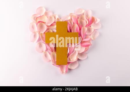 Über dem gelben christlichen Kreuz auf rosafarbenen Rosenblättern in Herzform auf weißem Hintergrund Stockfoto