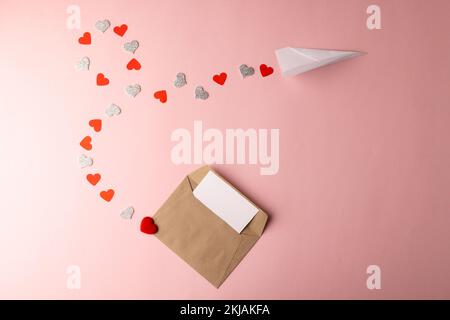 Offener Umschlag und Papierflugzeug mit Herzspur auf pinkfarbenem Hintergrund mit Kopierbereich Stockfoto
