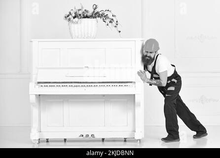 Mover runzelt die Stirn, während er schweres Klavier bewegt. Ein müder Kerl verlegt Sachen in der Wohnung, isoliert auf weißem Hintergrund. Hausdekorationskonzept Stockfoto