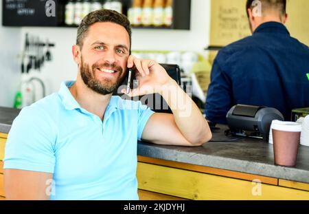 Mann Mobile Conversation Café Barista Hintergrund. Trinken Sie Kaffee, während Sie warten. Kaffee zum Mitnehmen für vielbeschäftigte Personen. Mann mit Smartphone bestellt Kaffee Stockfoto