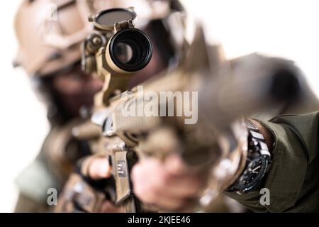 Ein Soldat mit taktischer Ausrüstung zielt mit Scharfschützengewehr auf den Feind. Oberflächlicher Fokus auf Gewehr. Isoliert auf weißem Hintergrund. Stockfoto