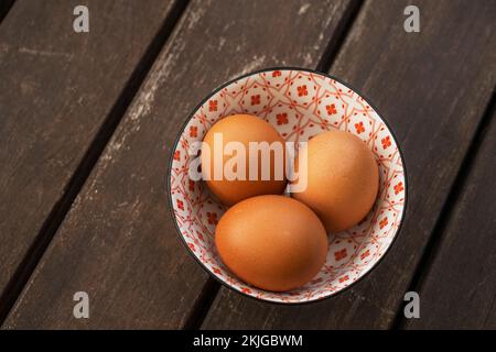 Frische braune Eier in einer wunderschönen porzellanschüssel auf braunen Akazienholzplanken Stockfoto