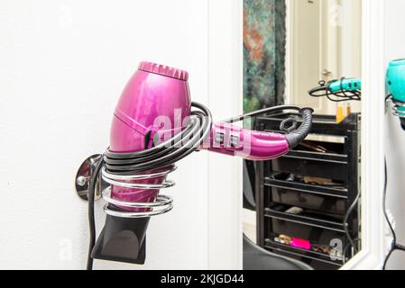 Rosafarbener Haartrockner mit Spiralkabel an einer Wandhalterung Stockfoto