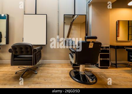 Hübsche schwarze Ledersofas in einem Schönheitssalon mit rechteckigen Spiegeln an der Wand und Kastanienfußboden Stockfoto