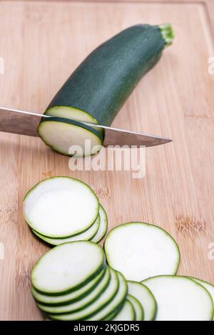 Ein Messer, das Zucchini auf einem Bambusbrett schneidet Stockfoto