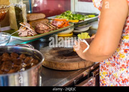 Vietnamesische Frau, die Zutaten für die Zubereitung von traditionellem Banh Me auf Street Food in Nha Trang zubereitet Stockfoto