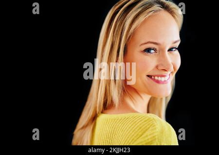 Sie beleuchtet jeden Raum. Studio-Porträt einer wunderschönen, jungen blonden Frau, die über ihre Schulter blickt, isoliert auf Schwarz. Stockfoto