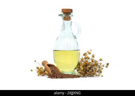 Leinsamenöl in Glasdekanter und Leinsamen in Holzschaufel in der Nähe von Flachsbäumen, isoliert auf weißem Hintergrund. Linum usitatissimum (Gemeiner Flachs) Stockfoto