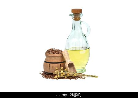 Leinsamenöl in Glasdekanter und Leinsamen in Holzschaufel in der Nähe von Flachsbäumen, isoliert auf weißem Hintergrund. Linum usitatissimum (Gemeiner Flachs) Stockfoto