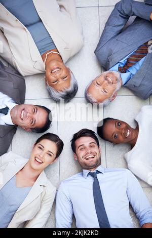 Kreis von Kollegen und Freunden. Hochwinkelporträt einer Gruppe von verschiedenen Geschäftsleuten, die im Kreis auf dem Boden liegen. Stockfoto