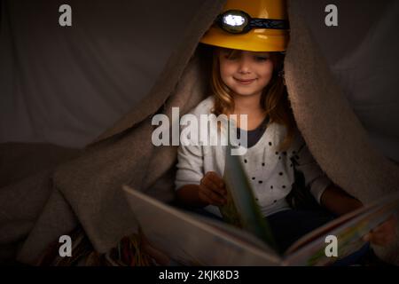 Heute ein Leser, morgen ein Anführer. Ein bezauberndes kleines Mädchen, das mit einem Scheinwerfer ihr Buch in einem Fort liest. Stockfoto