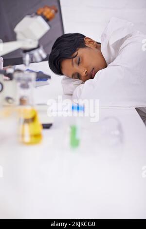 Ich mache Mittagsschlaf. Eine wunderschöne junge Wissenschaftlerin, die in ihrem Labor auf ihrem Schreibtisch schläft. Stockfoto